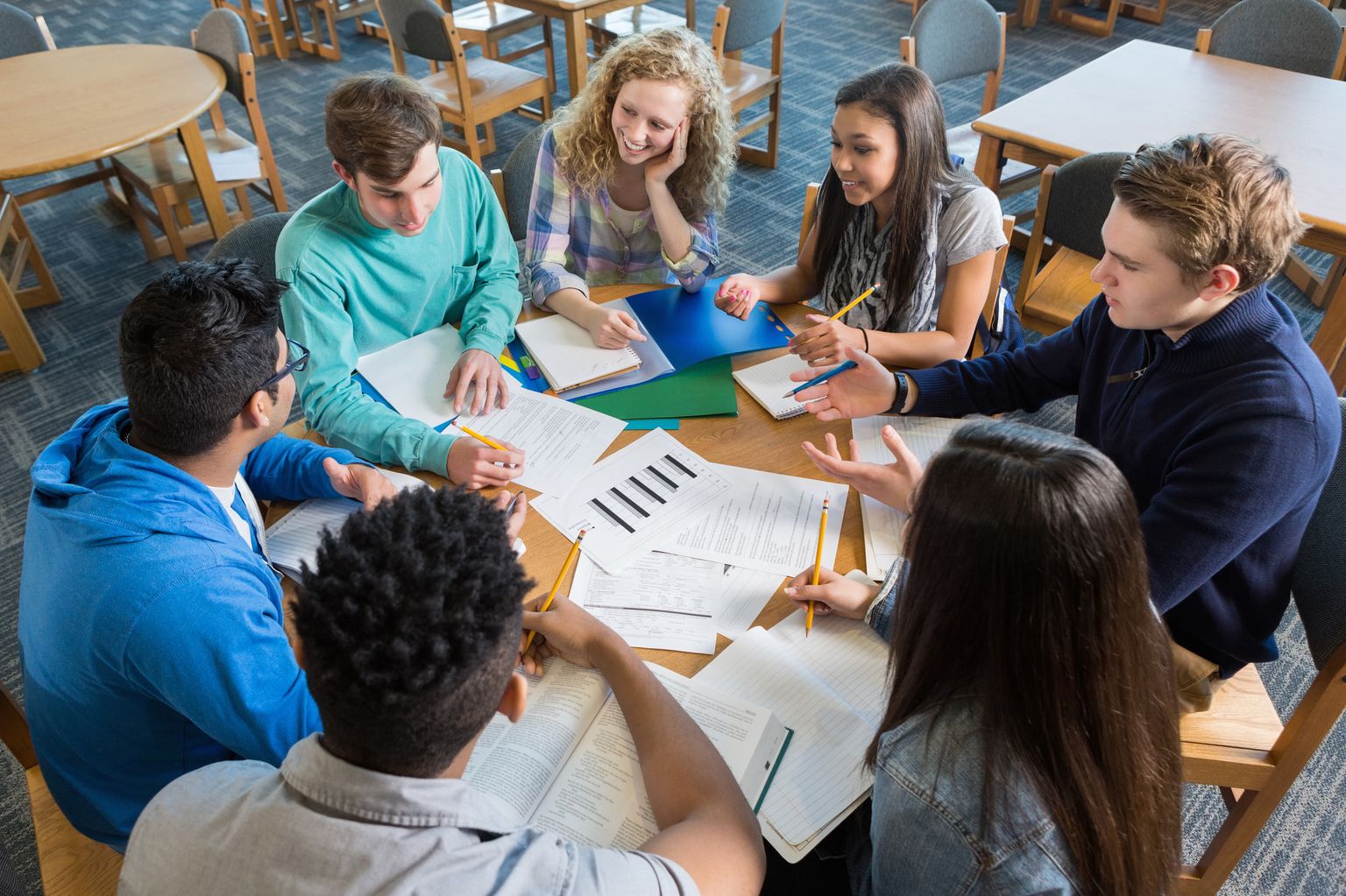  A group of high school students sit around a table in the library engaged in a respectful discussion about their studies.