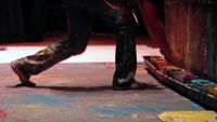 An artist is working on paint. There are so many colors of paint on the floor.