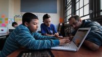 Teacher is helping the students work on the computer in a classroom.