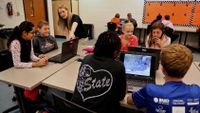 Teacher is guiding her students on how to play a game on computers.