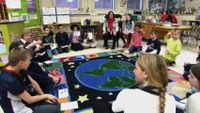 Students and teachers sitting on the classroom floor talking to each other.