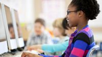 Young African American girl smiling while typing on computer keyboard.