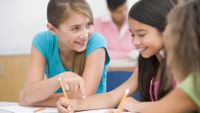 Three elementary school girls talking about an assignment in a classroom.