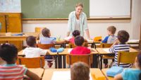 Smiling teacher facing class and talking to young elementary students.