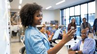 African American woman at whiteboard leading a meeting.