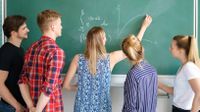 A group of students watching a teacher draw a graph on a blackboard.