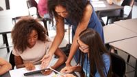 Teacher helping two middle school students with an assignment on a tablet computer.