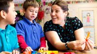 Smiling elementary teacher counting with two students in the classroom.
