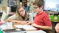 Elementary school teacher helping student in classroom.