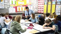 Teacher engaging with a group of high school students in the classroom.