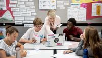 Teacher helping a group of teenage students in the classroom.
