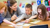 Teacher helping a group of kindergarten students with a project.
