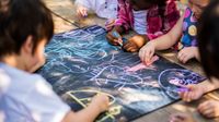 Preschool students drawing together with chalk on a large slate board