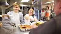 Two students serving free meals to homeless people at a free dining room