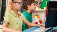 Two elementary students playing videogames on PCs