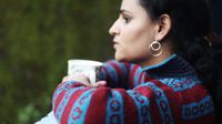 Woman looks thoughtfully out of a window with a cup of coffee in her hand
