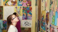 A middle school student attending a student art show, looking at her classmates' art on the wall