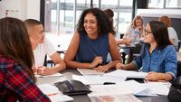 A teacher talking to her high school students at a table in a classroom