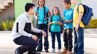 Teacher kneeling next to four elementary school students, smiling