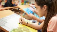 Student making a watercolor painting on a drawing table in art class