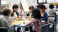 A group of five kindergarten students sitting at a table together, working with blocks in different shapes and sizes