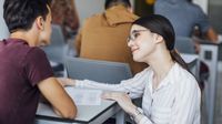 A teacher talks to her student while kneeling next to his desk