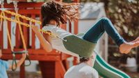 A young girl swinging on the swings at a playground