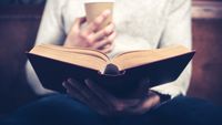 A man reading a book with a cup of coffee in his hand
