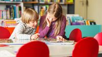 Two kids of different grade levels reading together in a library