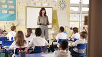A teacher stands at the front of an elementary class giving a lesson