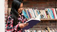 A student reading a book in front of a bookshelf