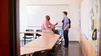 A teacher and a student talking after class, smiling and looking relaxed
