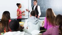 A math teacher working with a student in front of a diverse class
