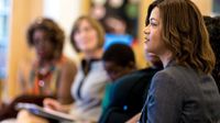 A female teacher is sitting in a room with other teachers. Everyone else is out of focus.