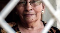 A closeup of an old woman's face with glasses framed by an outline of a white diamond shape.