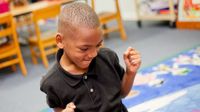 A young boy in a black shirt has his elbows against his sides and his hands raised in fists of excitement.