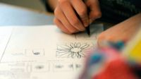A closeup of a student's hand drawing flowers on a piece of paper with pen.