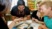 Three teenagers and an adult are sitting around a table, looking at a lot of pins standing up in a pan, smiling.