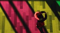 An aerial shot of a girl in a coat holding a cell phone up to her face. She's standing on a floor that's pink, yellow, and green from the lights shining down on it.