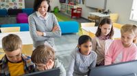 Two boys, three girls in front of computers with teacher standing behind them smiling