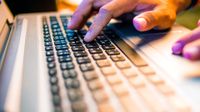 A closeup of a person's hands on a laptop keyboard.
