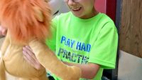 A young boy in a bright green shirt and glasses is smiling, holding a stuffed lion doll, looking straight into its face