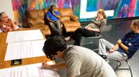 Five teachers in the lounge in discussion while one takes notes