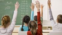 Several students—both female and male—earnestly raise their hands in a classroom.