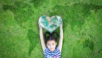 Young girl lying down, smiling, in the grass with heart-shaped globe above her head.