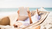 Woman on the beach reading and lounging in a hammock.