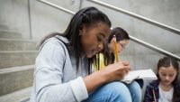 Students sitting and writing on stairs outside their school.