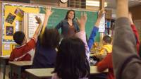 Teacher standing in front of class with students' hands raised