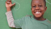 A photo of an elementary-school boy in front of a green chalkboard, smiling.