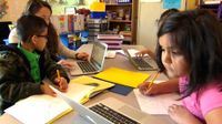 Teacher working with young students on laptops